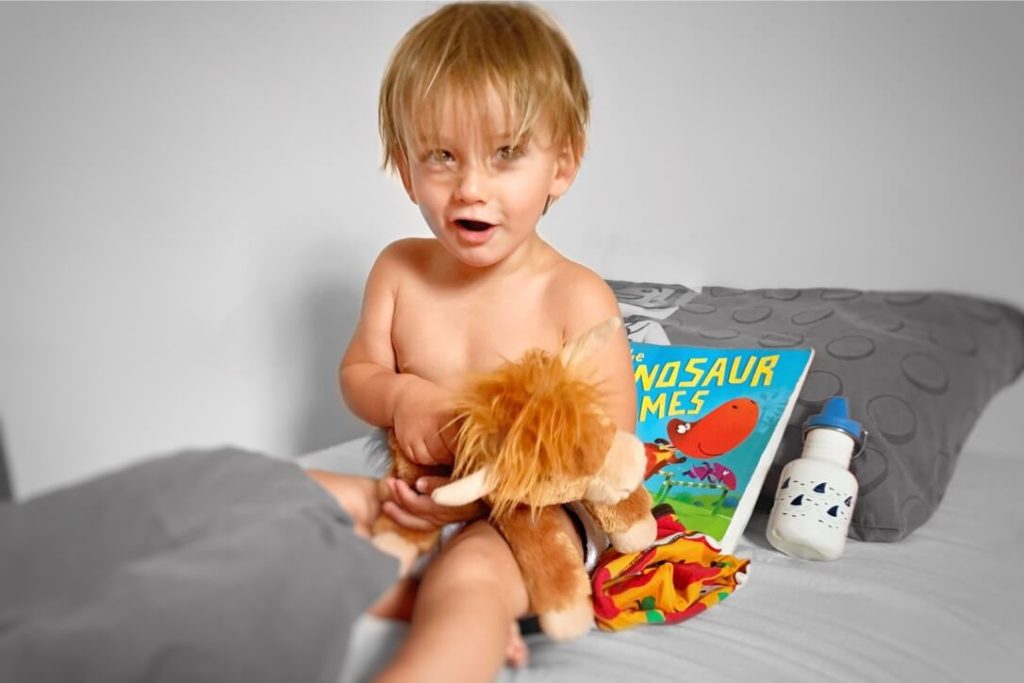 Toddler sat in bed, with toy, book and drink